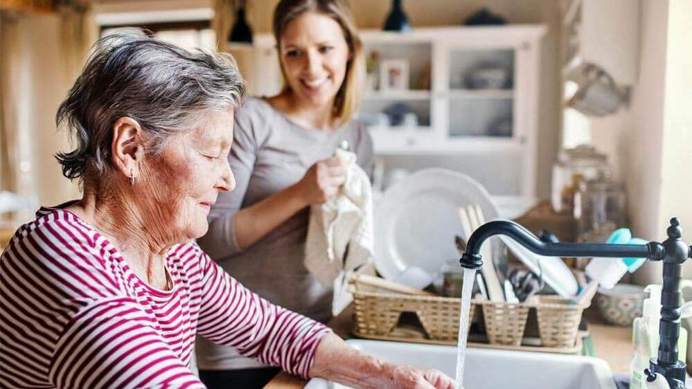 Wohnformen im Alter_ Seniorin mit mit ihrer Enkelin zu Hause beim Geschirr abwaschen