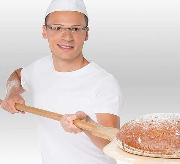 Ein Bäckermeister präsentiert stolz sein frischgebackenes Brot - Münchener Verein Glasversicherung