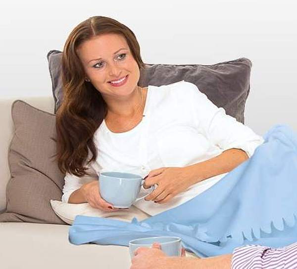 Frau liegt zugedeckt auf dem Sofa und trinkt Tee mit einem Mann - Münchener Verein Krankentagegeldversicherung