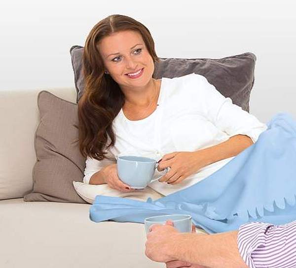 Frau liegt zugedeckt auf dem Sofa und trinkt Tee mit einem Mann - Münchener Verein Krankentagegeldversicherung