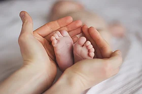 Bild von zwei H&auml;nden, die Kinderf&uuml;&szlig;e umschlie&szlig;en.