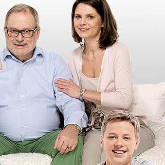 Älterer Herr sitzt auf dem Sofa umgeben von seiner Familie - Münchener Verein Private Pflegeversicherung