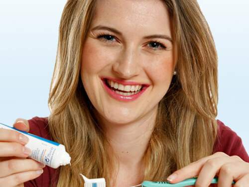 ZahnGesund - Junge Frau mit strahlendem Lächeln hält Zahnbürste und Zahnpaste in der Hand.