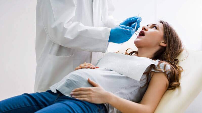 Zahnschmerzen in der Schwangerschaft-Schwangere Frau liegt auf dem Zahnarztstuhl und wird untersucht.