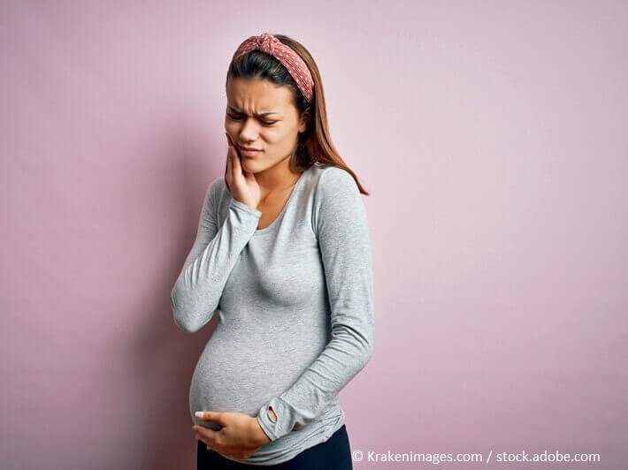 Zahnschmerzen in der Schwangerschaft_Junge, schwangere Frau mit schmerzverzerrtem Gesicht hält sich die Wange