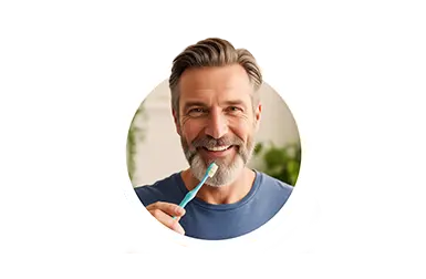 Mann mittleren Alters lächelt in die Kamera und hat eine Zahnbürste in der Hand. Er hat kurze Haare und einen Bart.