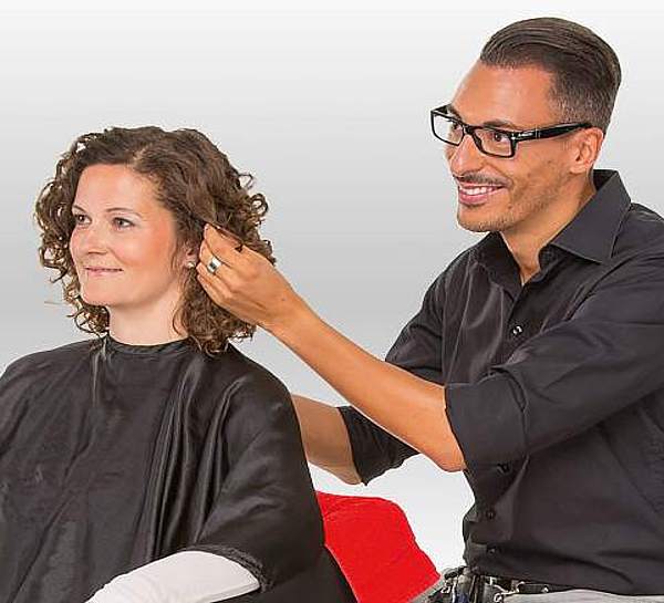 Freundlicher Friseur berät seine Kundin, die auf dem Friseurstuhl sitzt - Münchener Verein Geschäftsinhaltsversicherung