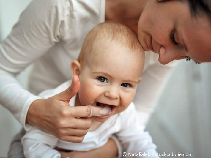 Zahnpflege Babys_Junge Mutter beugt sich über ihr Baby und massiert das Zahnfleisch.