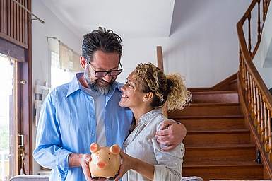 Bild eines Paares, das sich anlacht und ein Sparschwein in der Hand h&auml;lt.