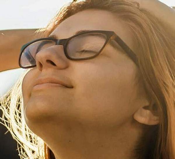 MV_Ratgeber- Junge_Frau mit Brille hat die Arme hinter dem Kopf verschränkt und genießt entspannt die Sonne.