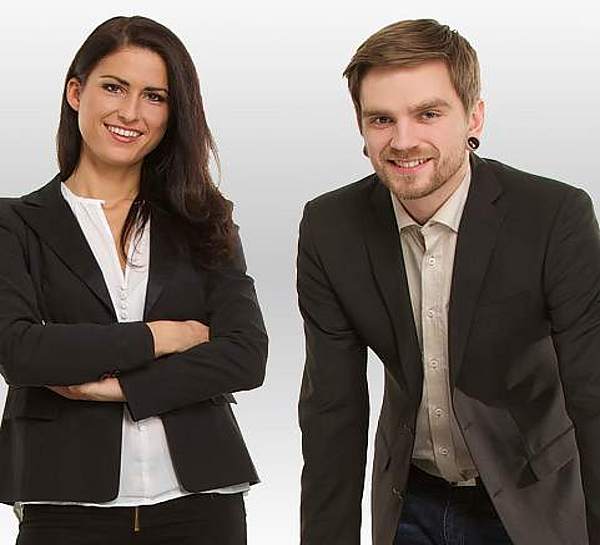 Mann und Frau in Anzug stehen nebeneinander und lächeln - Münchener Verein Firmenrechtsschutz