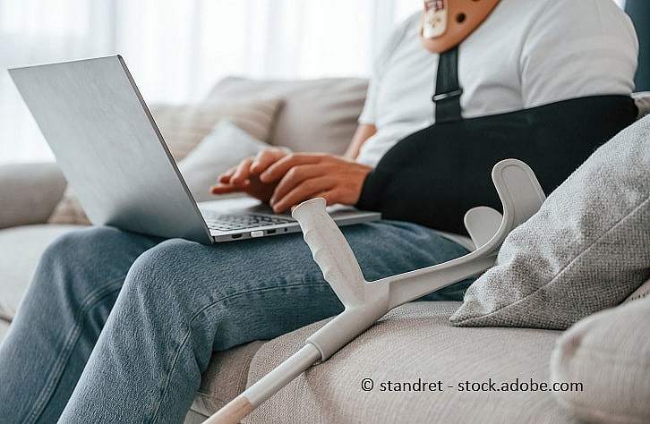 Bild einer Person, die mit gebrochenem Arm und Laptop auf der Couch sitzt.