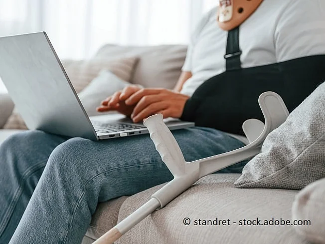 Bild einer Person, die mit gebrochenem Arm und Laptop auf der Couch sitzt.