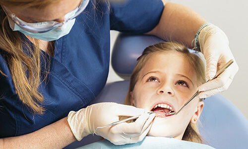 Kleines Mädchen sitzt im Zahnarztstuhl und lässt ihre Zähne untersuchen - Beste Zahnvorsorge mit der Deutschen ZahnVersicherung