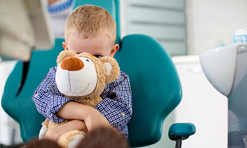 Kleiner Junge sitzt auf einem Zahnarztstuhl und drückt seinen Teddy ins Gesicht - Hypnosebehandlungen mit der privaten Zahnzusatzversicherung