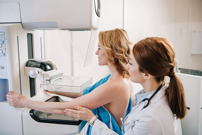 Eine junge Röntgenassistentin führt bei einer Patientin eine Mammographie-Untersuchung am Röntgengerät durch.