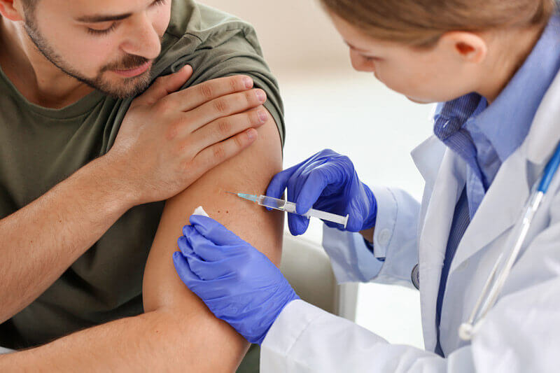 Eine Ärztin impft einen jungen Mann am linken Oberarm.