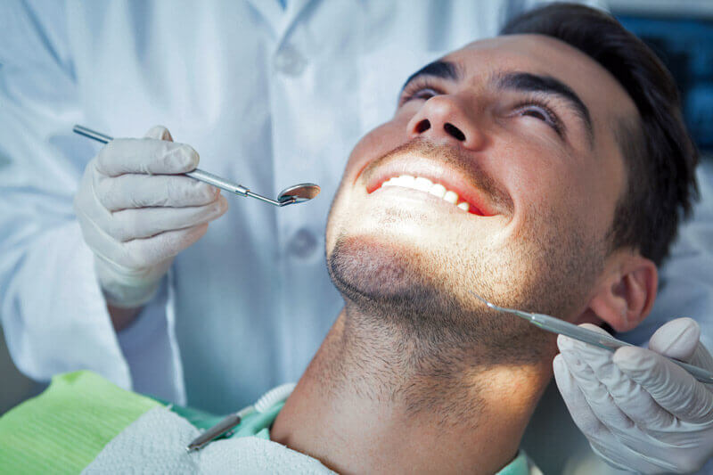 Nahaufnahme eines Mannes, der seine Zähne vom Zahnarzt untersuchen lässt.