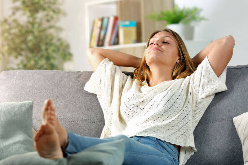 Stress schwächt das Abwehrsystem - Junge Frau sitzt entspannt auf einem Sofa.