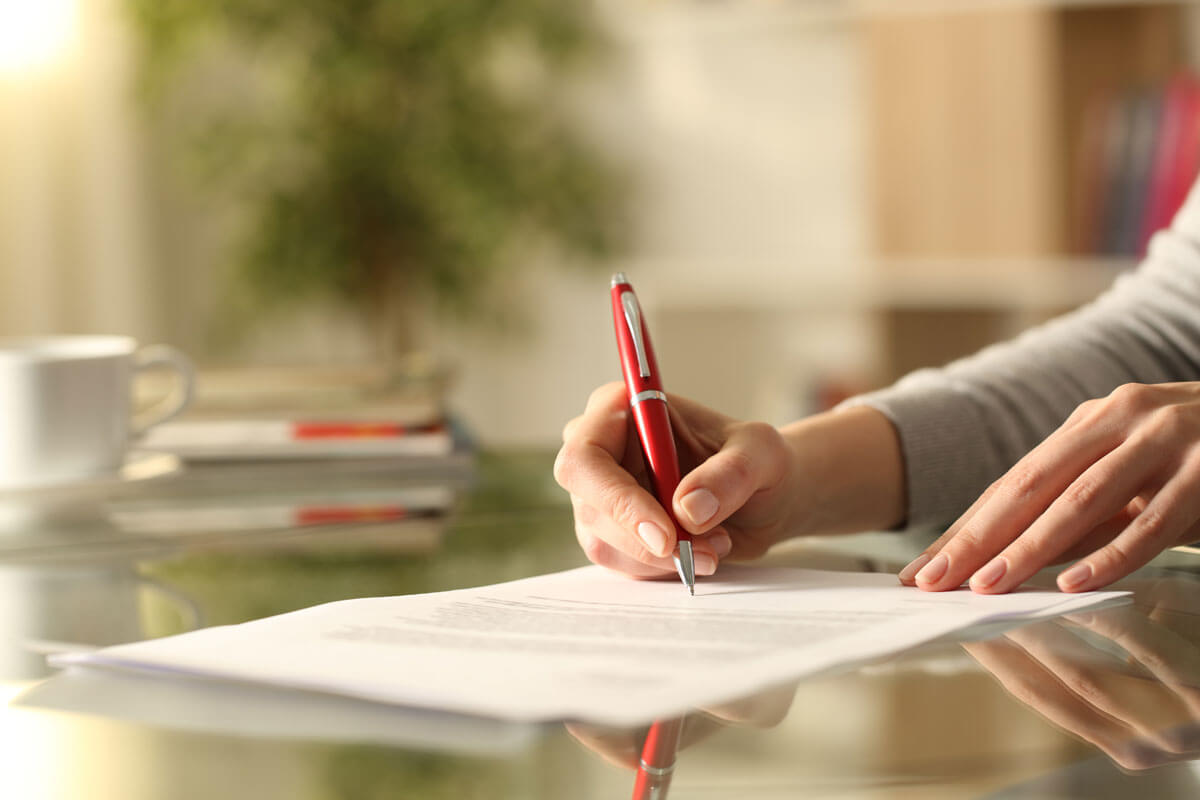 Patientenverfügung und Betreuungsvollmacht - Frau unterschreibt Dokument mit Stift ihrem Schreibtisch zu Hause