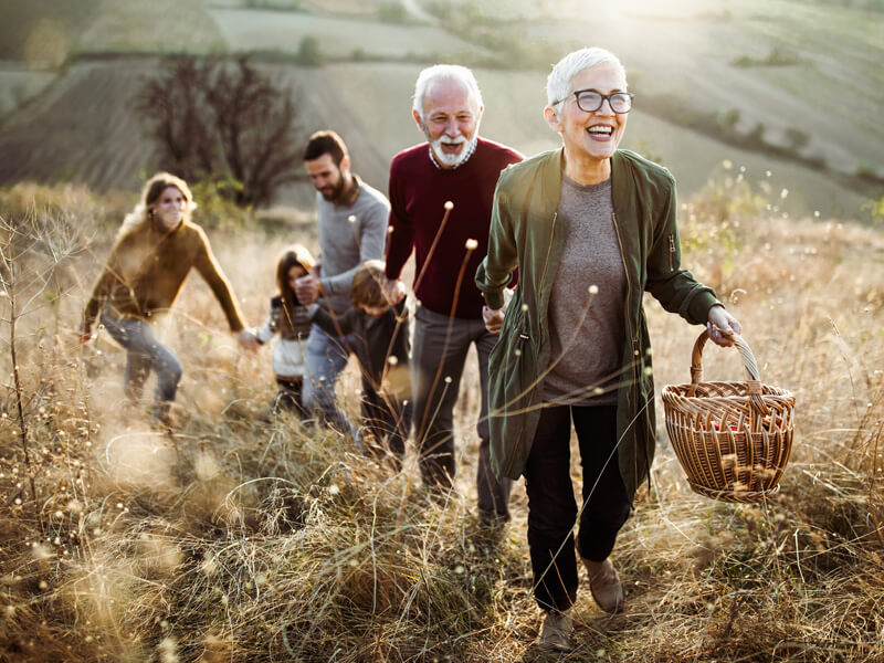 Ratgeber Pflege - Glückliche Seniorin führt ihre Familie zu perfektem Picknickplatz auf dem Hügel