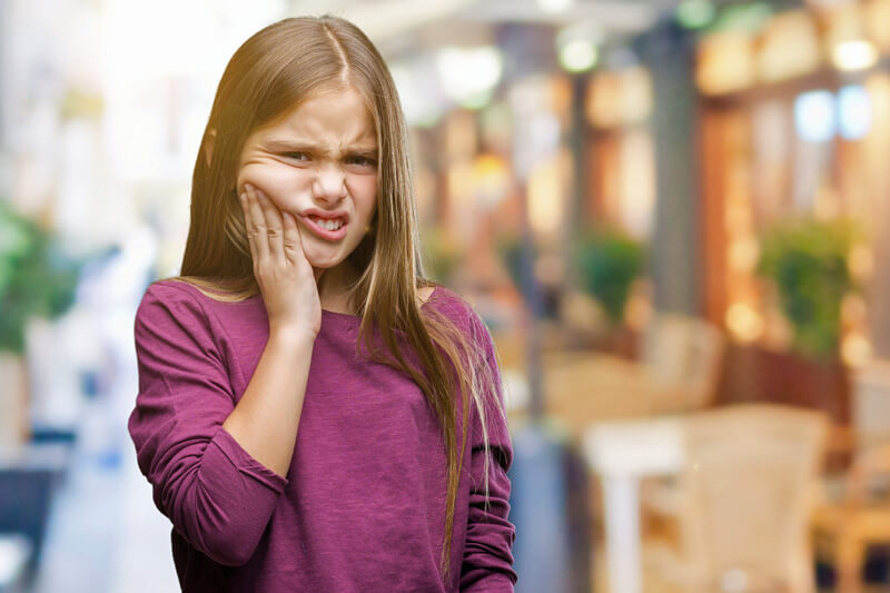 Hausmittel Zahnschmerzen Kinder -  Kleines Mädchen hält sich schmerzverzerrt die Wange
