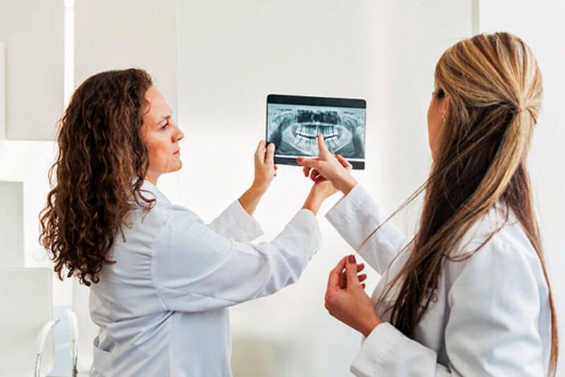 Implantat oder Brücke_Zahnärztin zeigt ihrer Kollegin etwas auf einem Röntgenbild.