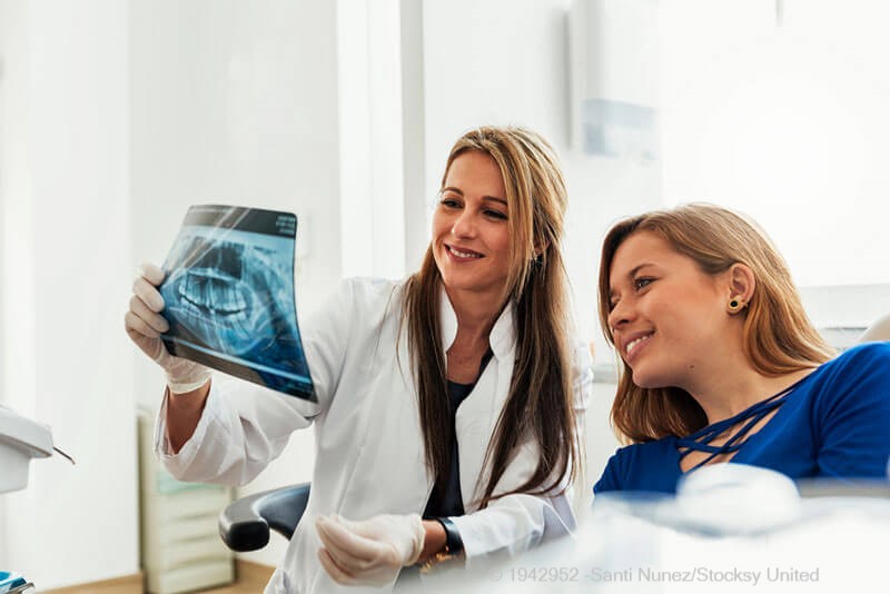 Implantat oder Brücke: Ärztin bespricht mit ihrer Patientin eine Röntgenaufnahme.