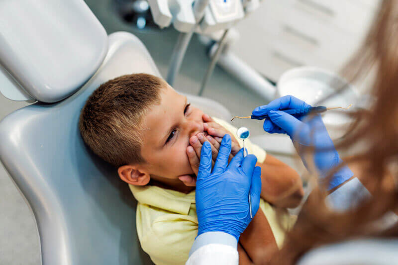 Kleiner Junge im Zahnarztstuhl, der sich aus Angst den Mund zuhält.