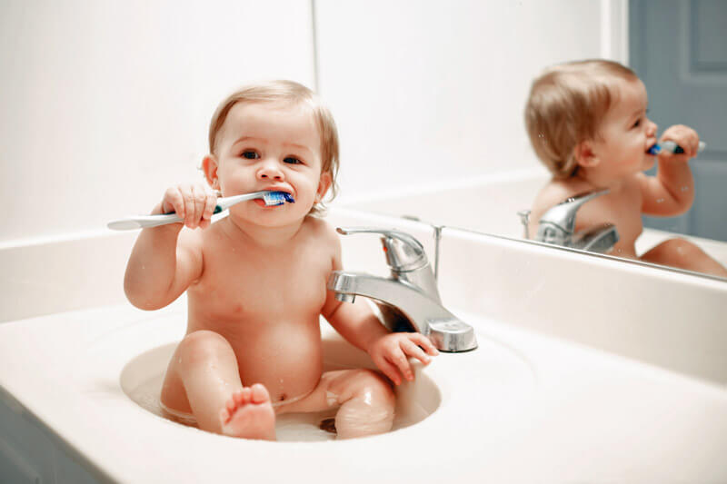 Zahnpflege Babys_Baby sitzt im Waschbecken und putzt sich die Zähne.