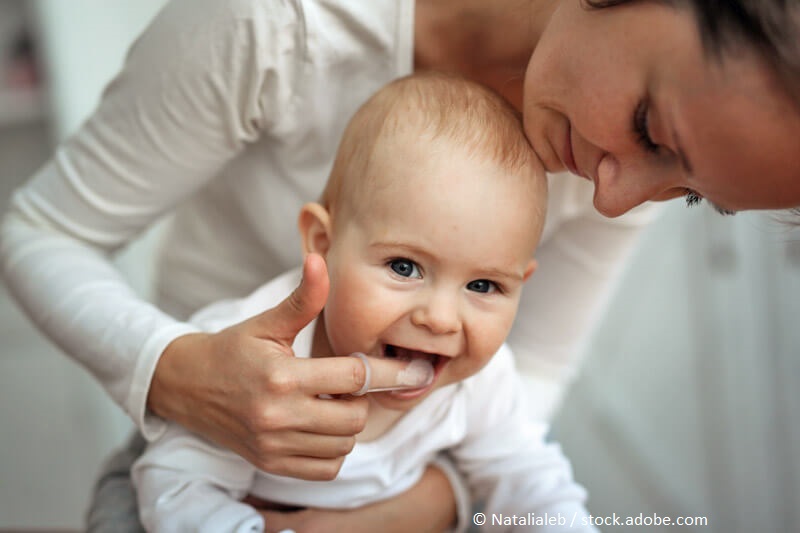 Zahnpflege Babys_Junge Mutter beugt sich über ihr Baby und massiert das Zahnfleisch.