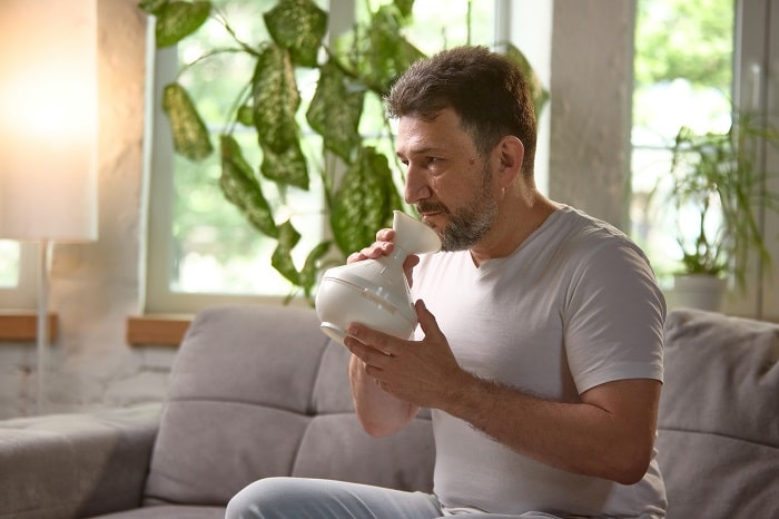 Bild eines Mannes auf einer Couch, der ein Inhalationsgerät verwendet.