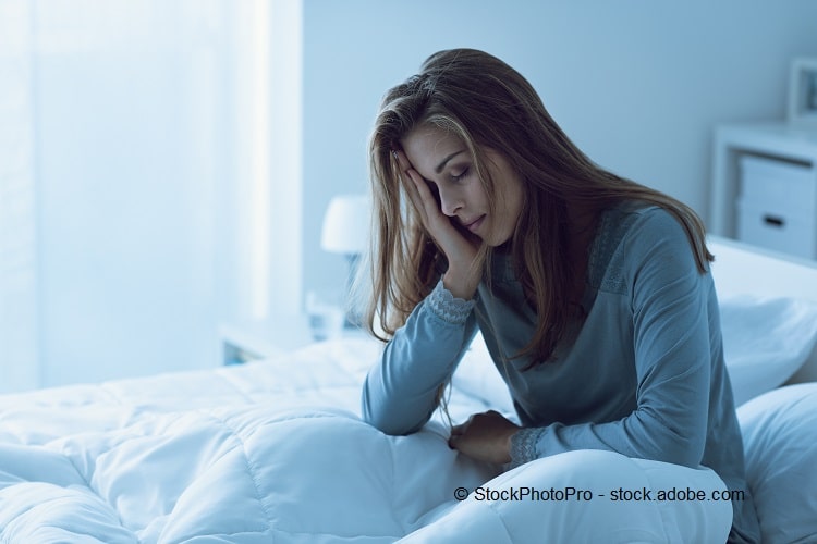 Bild einer Frau, die auf dem Bett sitzt und ihren Kopf auf ihren Arm stützt.